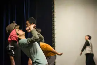 Actors in rehearsal clothes reaching and stretching together in a bare studio