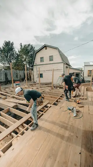 A crew framing a floor beside a house