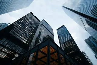 Glass office towers seen from below against a cloudy sky