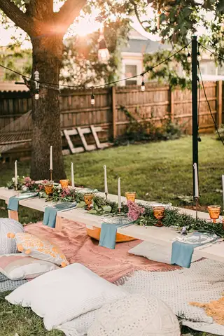 A low backyard table with cushions and candles laid out under a tree