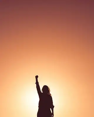 Silhouette of a woman raising a fist against an orange sky