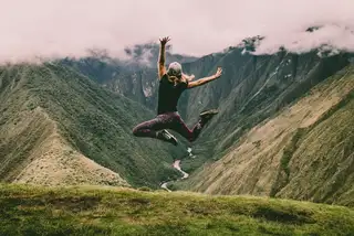 A person leaping in the air above a green mountain valley