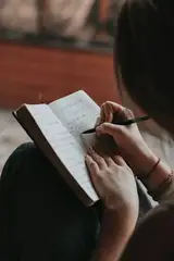 A woman writing in a small notebook held on her knee