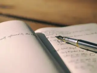An open notebook with handwritten notes and a silver fountain pen on the page