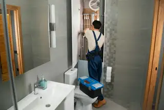 A plumber carrying a toolbox into a bathroom