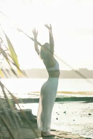 A backlit woman stretching her arms overhead on a beach, washed out by sun glare
