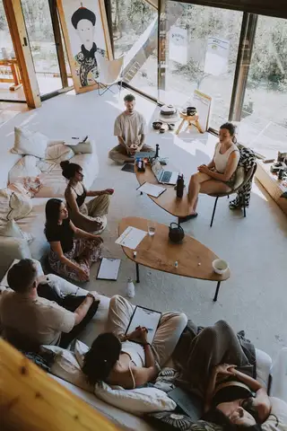A small group on cushions and sofas around a low table in a bright room with tall windows