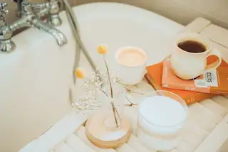 A candle, a cup of tea and dried flowers on a wooden tray in soft daylight